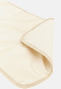 Beige tygmatta med en slät textur, försedd med en sydd kant. Mattan är delvis vikt, vilket visar dess lätta design.