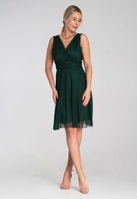 Dunkelgrünes, knielanges Kleid mit V-Ausschnitt und tailliertem Oberteil. Es hat einen strukturierten Tüllrock, ärmelloses Design und eine Wickeldetail an der Taille.