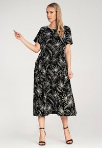 Black dress with floral white embroidery, short sleeves, a knee-length skirt, and a side tie detail, paired with black strappy heels.