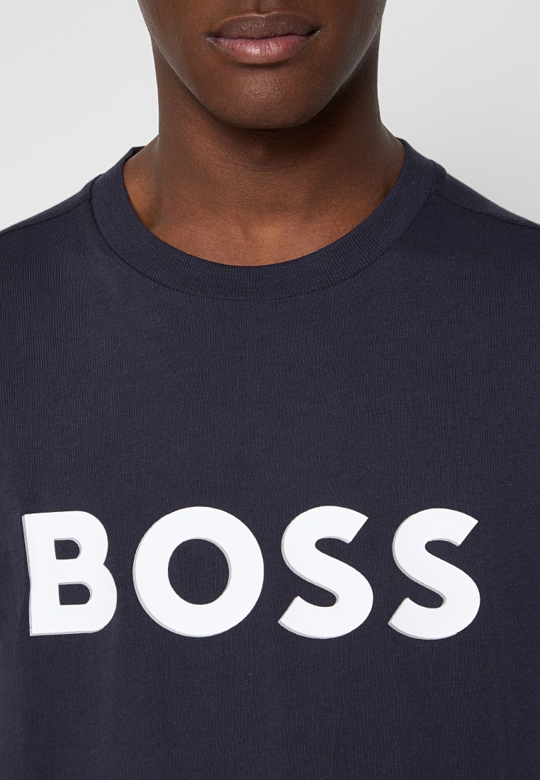 T-shirt bleu marine en coton avec un col rond, arborant en grand les lettres blanches "BOSS" sur la poitrine. Texture lisse, coupe décontractée.