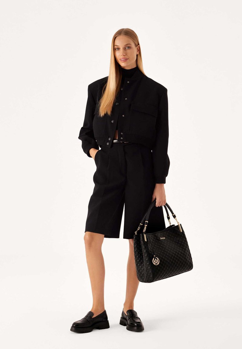 Giacca nera cropped con due tasche frontali, top a collo alto, pantaloni bermuda neri e borsa testurizzata con hardware dorato. Mocassini neri.