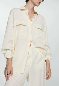 Lichtgele, oversized overhemd met knopen, voorzien van twee borstzakken en opgerolde mouwen. Gemaakt van een zachte, lichte stof.