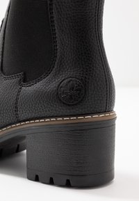 Bottine noire avec un dessus en cuir texturé, des panneaux latéraux élastiques, un bout rond et un talon empilé avec une semelle en caoutchouc profilée.