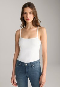 Witte spaghetti-top met vierkante halslijn, gemaakt van zachte stof. Draagt met blauwe skinny jeans, wat een casual, minimalistische stijl laat zien.