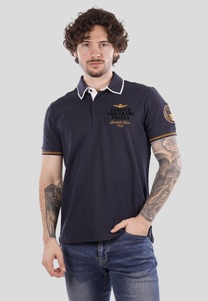 Polo shirt blu navy con colletto bianco e dettagli gialli. Presenta il logo ricamato "Frecce Tricolori Italia" in oro. Maniche corte, design aderente.