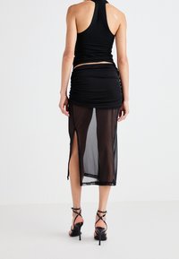 Schwarzes Haltertop kombiniert mit einem schwarzen Mesh-Rock, der Raffung, Seitenschlitze und Spitzenbesatz aufweist. Stilettos mit verzierten Riemen vervollständigen den Look.