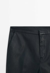 Pantalon en similicuir noir à la texture lisse, doté d'une coupe droite, d'une ceinture et de poches latérales. Coutures détaillées visibles.