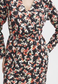 Robe portefeuille fleurie avec de longues manches, arborant une base noire et un motif vif de rouge, blanc et vert dans un tissu doux et léger.