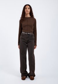 Brown ribbed long-sleeve top paired with high-waisted, dark jeans and a studded belt. Soft texture and relaxed fit throughout.