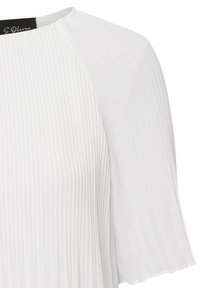 Blouse blanche plissée avec des manches courtes évasées et un col rond. Le tissu a une texture douce ; des lignes verticales subtiles mettent en valeur le design.