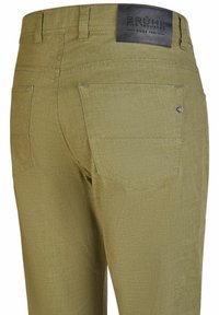 Olivenfarvede bukser med baglommer, bæltestropper og et sort lædermærke med teksten "Brühl Fine Trousers Since 1923" på taljen.