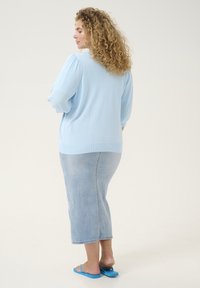 Light blue knitted sweater with loose-fit sleeves, paired with a light denim midi skirt and blue flip-flops. Textured, breathable fabric.