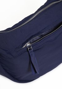 Marineblaue Stofftasche mit glatter Textur, ausgestattet mit einem silbernen Reißverschluss und einem kleinen Stofftab für besseren Halt. Funktionales und minimalistisches Design.