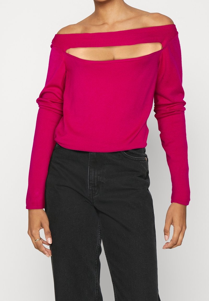 Pull magenta à épaules dénudées avec manches longues, présentant un design découpé sur la poitrine et un tissu lisse et léger.