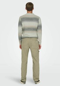 Grå og beige stribet striktrøje med rund hals, parret med grønne kordfløjl bukser med baglommer og slim fit. Sorte sneakers synlige.
