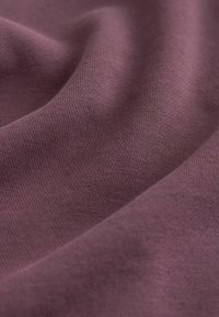 Puha, matt felületű textil, gazdag mályvaszínnel, finom, egyenletes kötésmintával és finom textúrával.