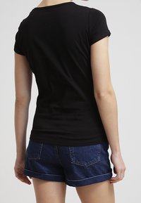 Camiseta negra de manga corta con escote redondo, diseño ajustado y textura suave, combinada con pantalones cortos de mezclilla con dobladillos enrollados.