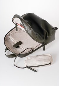 Olijfgroene leren rugzak met een ritsluiting, voorzien van een gemusterde beige voering en een afneembare beige tas.
