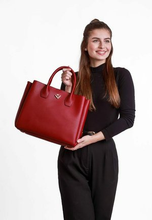 Červená kožená kabelka s dvěma vrchními držáky, obdélníkový tvar a zlatý logový akcent. Hladká textura, minimalistický design, žádný viditelný hardware.