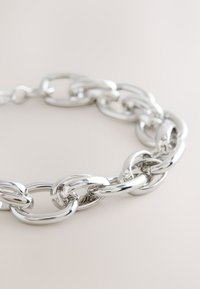Silver metal chain bracelet featuring interlocking oval and round links with a smooth, shiny texture. Reflective finish enhances visual appeal.