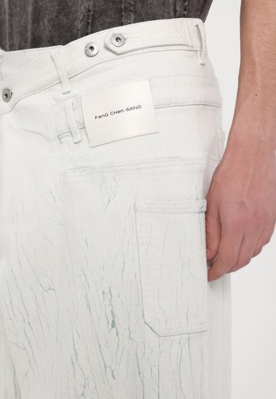 Pantalones de mezclilla blancos con una superficie texturizada que presenta patrones de craquelado azul claro, cinco bolsillos y una etiqueta blanca que dice "Feng Chen WANG."