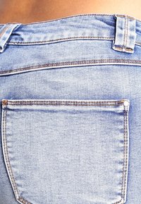 Ljusblå denimjeans med en bakficka som har kontrasterande sömmar. Tyget har en slät yta med subtila blekningar.