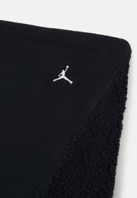Svart fleece-pledd med en kontrasterende teksturkant. Har en hvit Jumpman-logo i øverste hjørne. Mykt og koselig materiale.