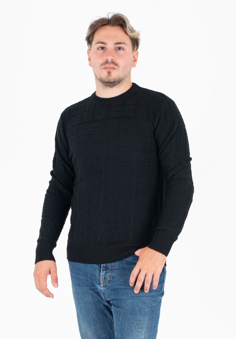 Czarny sweter o teksturowanej powierzchni z wzorem w kratę, z okrągłym dekoltem i prążkowanymi mankietami. Połączony z niebieskimi dżinsami. Model stoi na tle białym.