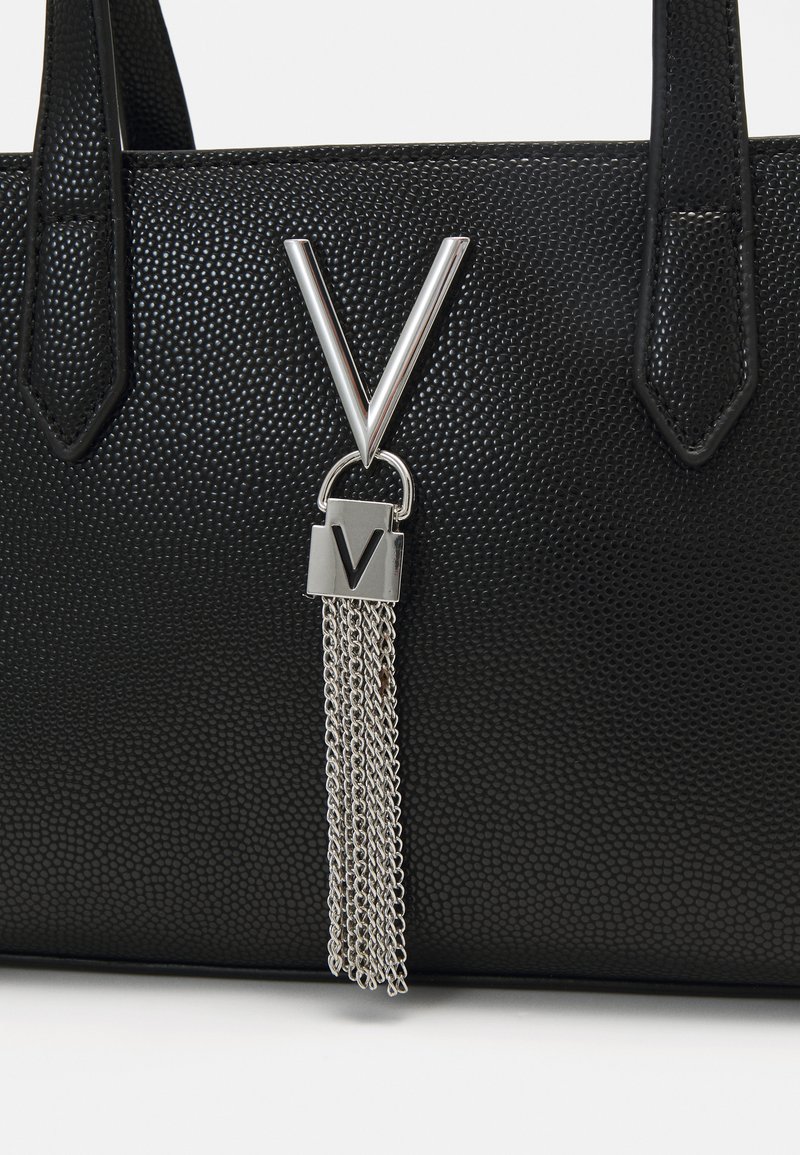 Schwarze handgefertigte Handtasche mit silbernem Zubehör, die mit einem dreieckigen Designdetail und einem Kettentassel-Anhänger versehen ist, der an einem Schloss befestigt ist.