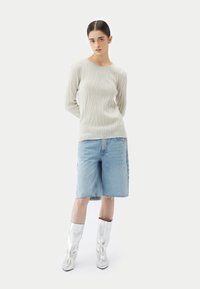 Pull gris clair texturé à manches longues, assorti à un short en denim bleu clair et des bottes argentées brillantes montant jusqu'aux genoux.