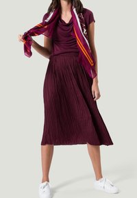 Gonna plissettata bordeaux abbinata a un top coordinato e una sciarpa a fantasia. Sneakers bianche completano il look. Tessuto dal tocco morbido.