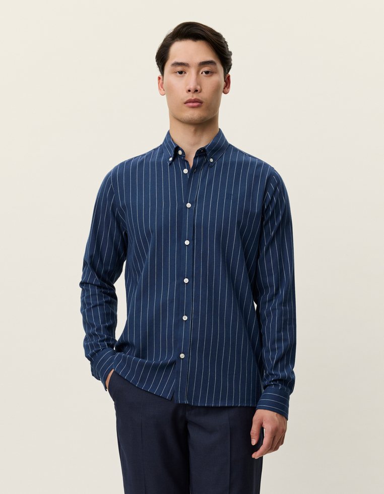 Sötétkék, hosszú ujjú ing, fehér függőleges csíkokkal, gallérral és gombos légzéssel, texturált anyagból készült.