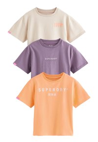 Tre kortärmade skjortor staplade: beige, lila och orange. Varje skjorta har en "SUPERDRY"-logotyp i en kontrasterande färg, rund hals och avslappnad passform.