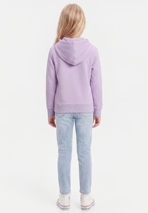 Barn med langt blondt hår iført en lavendel hættetrøje, lyseblå jeans og hvide høje sneakers, set bagfra på en hvid baggrund.
