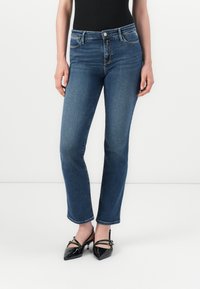 Mørkeblå denimjeans med en tettsittende design, medium høyde i livet og subtile slitasjer. Kombinert med sorte blanke høyhælte sko.