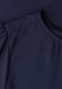 Gros plan sur un tissu bleu marine montrant une épaule bouffante et une couture au niveau de l'encolure d'un vêtement.