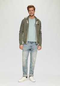Grauer Zip-Hoodie mit hellen Akzenten, blaues T-Shirt, hell ausgewaschene Jeans und weiße Sneaker mit schwarzen Akzenten. Lässiges Outfit.