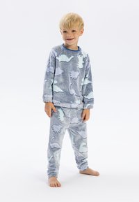 Pyjamas en polaire gris clair avec une texture douce, ornés de motifs de dinosaures pastel. Le haut a des manches longues et un col bleu.