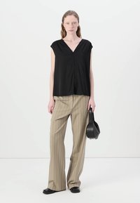 Black, short-sleeved top with a V-neck, paired with beige striped, wide-leg pants. Model holds a small black handbag.