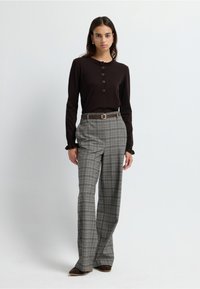 Top marrón de manga larga con cuello con volantes y detalles de botones, combinado con pantalones de cuadros grises de cintura alta y cinturón marrón.