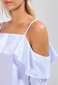 Světlomodrý pruhovaný top se spadlými rameny, s volánkovým výstřihem a tenkými ramínky, vyrobený z hladkého materiálu, s uvolněným střihem.
