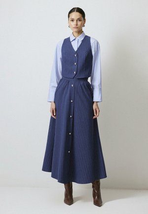 Marineblauwe gestreepte jurk met een getailleerde vest en een brede rok. Beschikt over zilveren knopen aan de voorkant en lange gestreepte mouwen. Bruine haklaarzen.