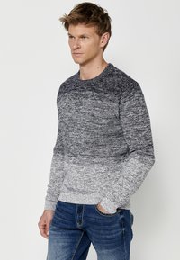 Grijze ombre gebreide trui met een geribbelde ronde hals en lange mouwen. Heeft een textuurpatroon dat van donkergrijs naar lichtgrijs overgaat.