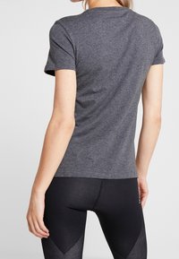 Szary t-shirt z krótkim rękawem wykonany z miękkiego materiału, z klasycznym okrągłym dekoltem i dopasowanym krojem, zestawiony z czarnymi legginsami o fakturowanej powierzchni.