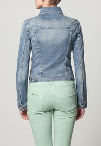 Jeansjacka med en ljusblå tvätt, strukturerad design och krage. Bärs med mintgröna byxor som har bakfickor och gulddetaljer.