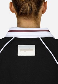 Μαύρο πουκάμισο πόλο με λευκό γιακά με μπορντό ρίγες και ορθογώνια ετικέτα μάρκας στο πίσω μέρος με το όνομα "pegador" σε �ανοιχτό χρώμα.