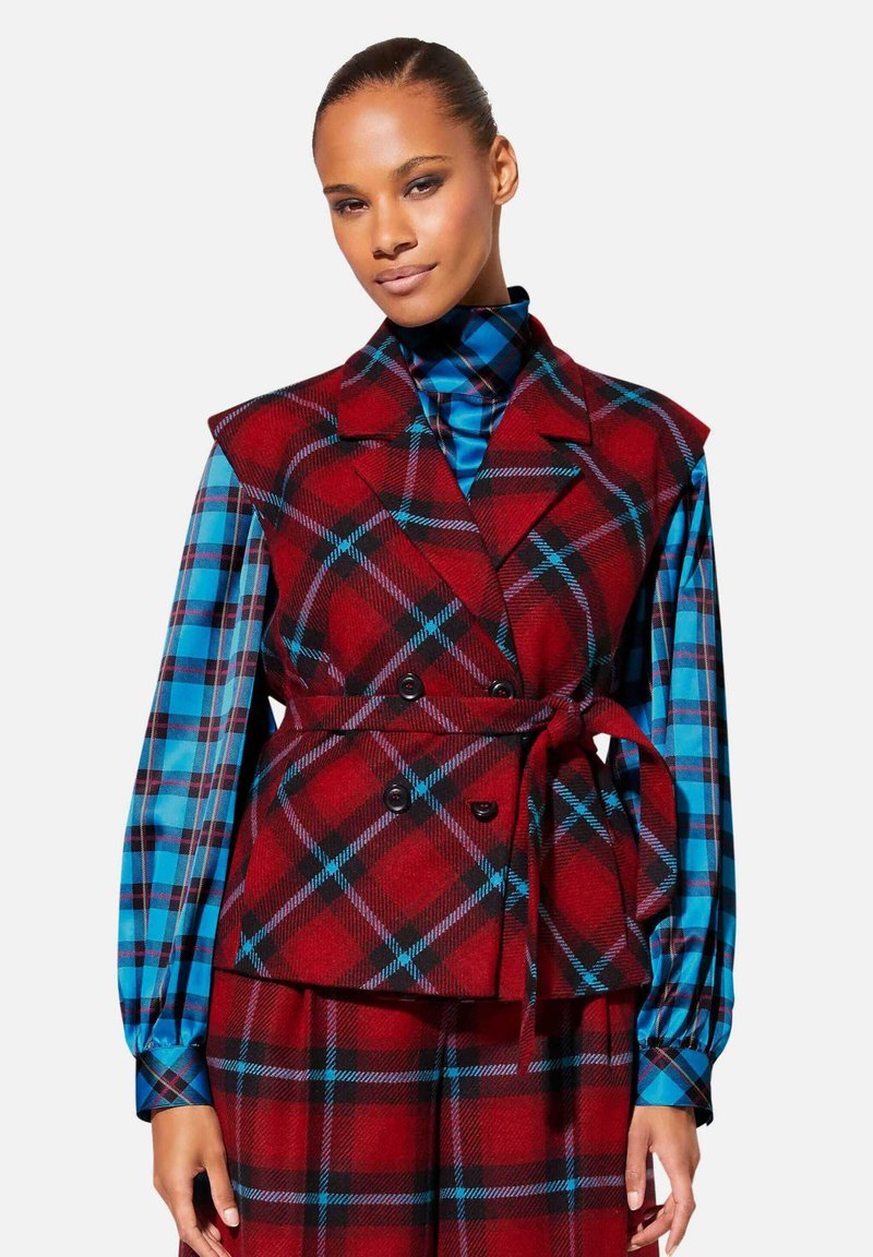 Rood geruite vest met een wikkeldesign, voorzien van een kraag en dubbelknopsluiting, gelaagd over een blauw-zwart geblokt shirt.