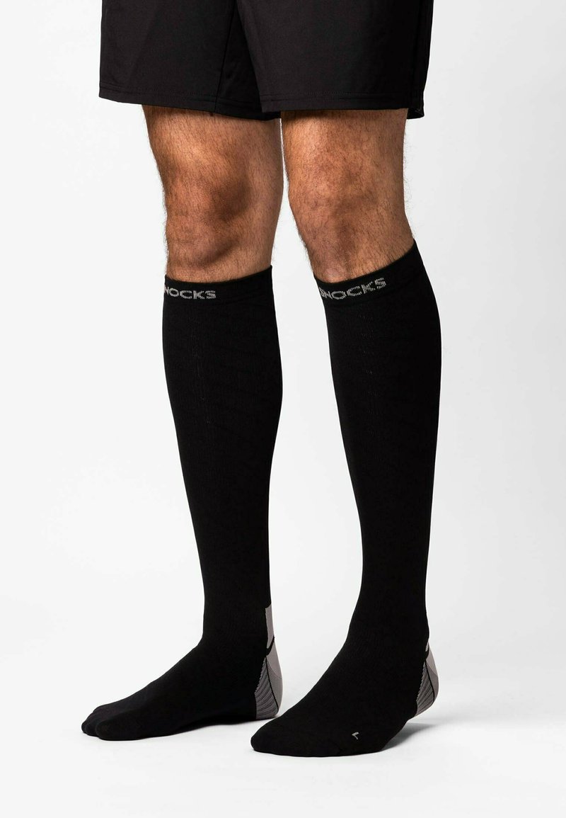 Knee-high black compression socks with a ribbed texture, featuring gray accents and branding along the top band, designed for performance.