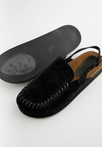 Fekete velúr slip-on cipő lekerekített orral, díszítő varrással a szélein és barna talpbetéttel. Lapos gumitalp a tapadásért.