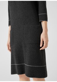 Šedé šatové šaty ze směsi vlny s volným střihem, tříčtvrtečními rukávy a dvěma předními kapsami. Ozdobené detaily světle šedého šití.